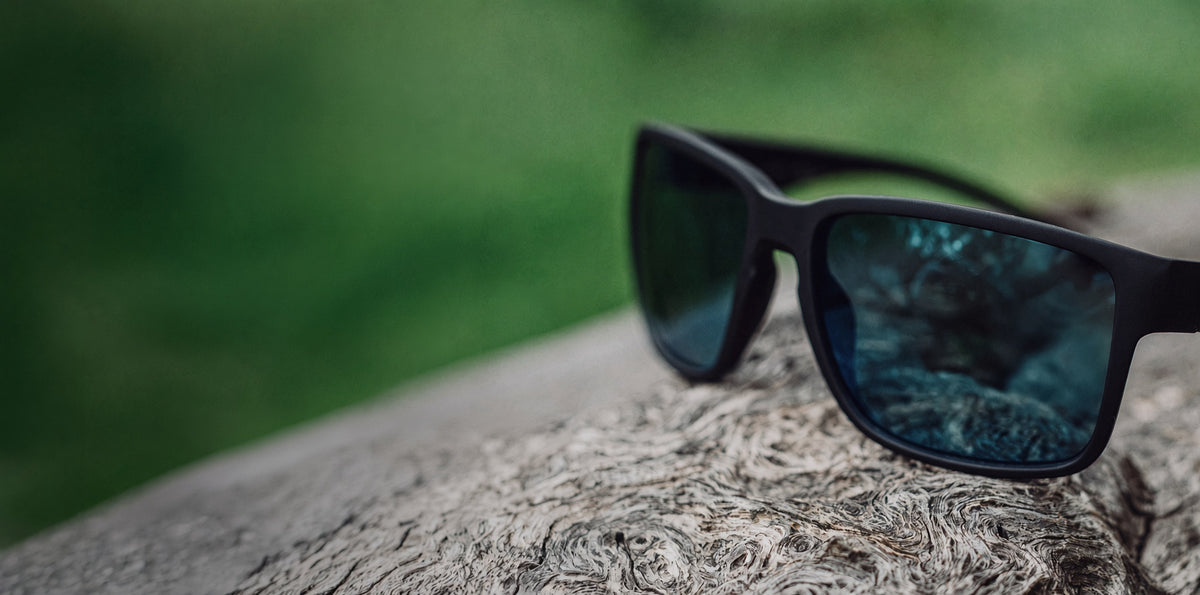 Black sunglasses with blue mirrored lenses resting on weathered wood